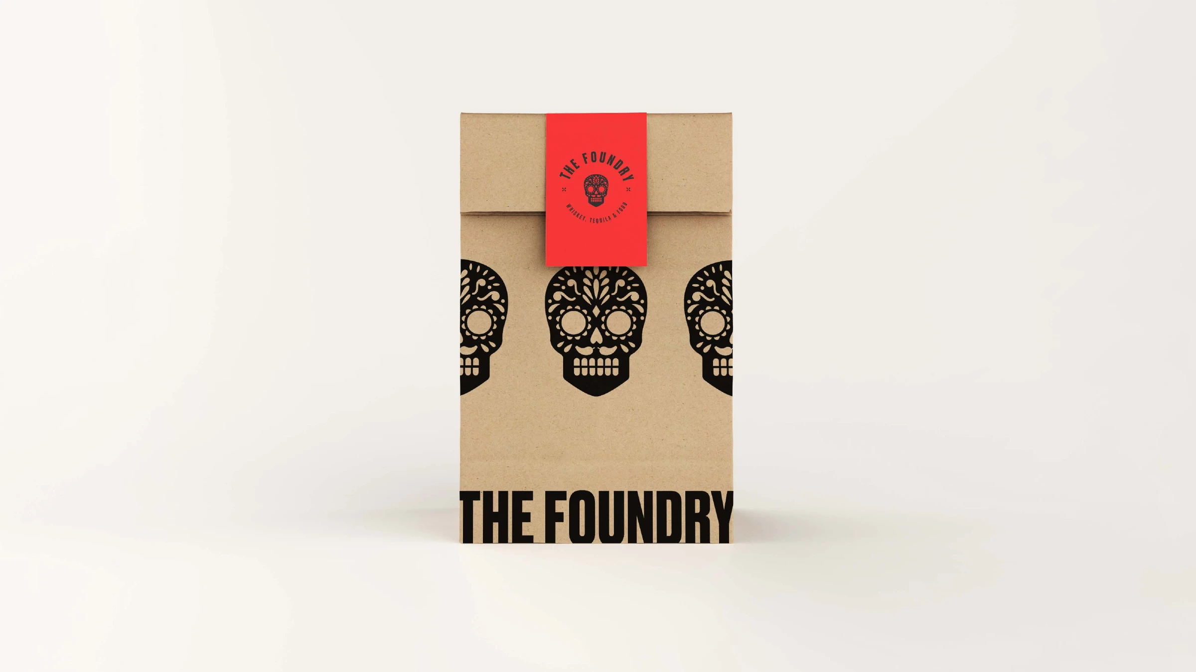 The Foundry kraft takeout bag printed with a row of black sugar skulls and a red seal